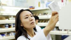 Pharmacist in a pharmacy looking at a piece of paper while holding it up to the light