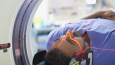 Person being rolled into an imaging machine with red lasers scanning their head 