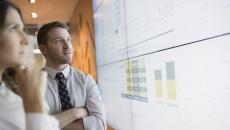 Two people standing in front of a large white board that has graphs on it