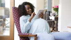 Pregnant person sitting in a chair, looking at a tablet