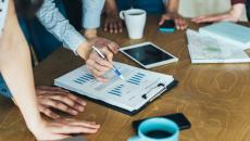 A close up of businesspeople gathered around a table looking at financial charts