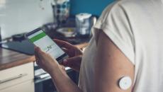 Woman checking glucose level with a remote sensor and mobile phone.