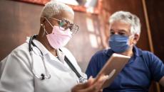 A doctor holding a tablet while talking to a patient. 