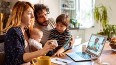 Parents with two young children talk to a provider through a video call on their laptop.