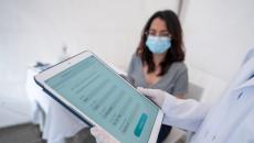 Person holding tablet in front of person wearing surgical mask