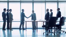 Group of three people on left, two people shaking hands in middle, three people standing behind office chairs on right