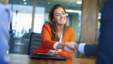 Person in an orange suit shaking hands with someone on the other side of a desk