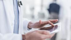 The body of a healthcare provider using a tablet while wearing a lab coat and stethoscope around their neck