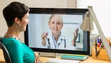 Person with green shirt talks with person on computer monitor in lab coat