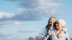 Person wearing a scarf on their head holding a child on their back with the sky behind them