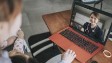 Person sitting down looking at a computer on a coffee table, talking to a healthcare provider