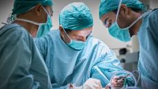 Surgeons in an operating room huddled around a patient on an operating table