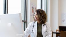 Healthcare provider with a lab coat on sitting at a desk and looking at a computer