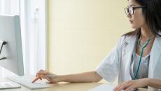 Healthcare provider sitting at a desk wearing a stethoscope around their neck and working on a computer