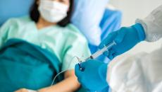 Healthcare provider putting medication into an infusion line with a patient lying in a bed