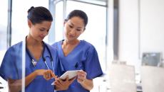 Two healthcare providers standing up while looking at one tablet