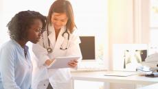 Healthcare provider standing over a patient sitting down while showing them a tablet 