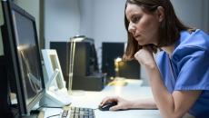 Healthcare provider sitting at a desk looking at a screen with their hand on the mouse