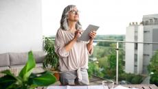 Person standing on a balcony looking at the sky with a tablet in their hand