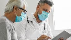 Healthcare provider and patient sitting next to each other wearing masks and looking at a tablet