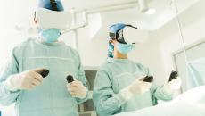 Healthcare providers in an operating room wearing an extended reality headset while standing over a patient