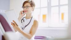 Healthcare provider looking at a tablet while wearing a white shirt and a stethoscope around their neck