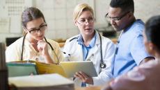 Three healthcare providers sitting together looking at a tablet together