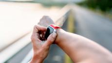 A person wearing a wearable device on their right wrist and touching the device with their left hand