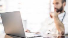 Healthcare provider sitting at a desk while wearing a stethoscope around their neck and looking at a computer