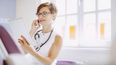 A doctor reading a patient's chart while discussing it with another doctor on the phone