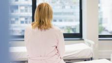 A woman sitting on a hospital bed with her back to the camera