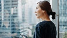 A person looking out a window holding a smartphone