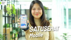 A person holding a mobile phone showing the Satusehat app